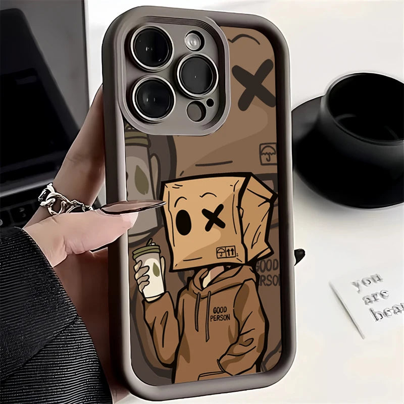 A person holds a phone with a custom case featuring a cartoon character wearing a paper bag with eyes and an "X" over one. The character holds a coffee cup and wears a hoodie labeled "Good Person."