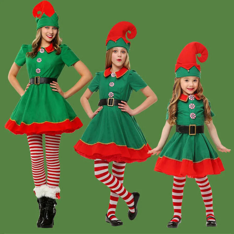 Three children in Christmas elf costumes with green dresses, red hats, and striped red-and-white stockings stand against a green background, smiling and posing festively.