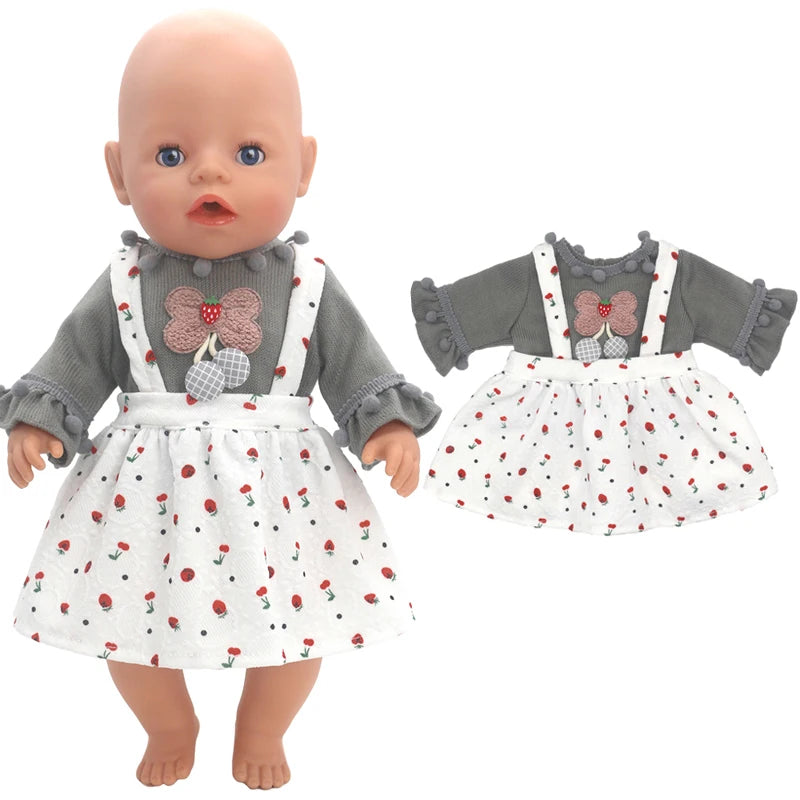 A doll wearing a gray top with pom-pom accents and floral overalls, featuring a decorative flower on the chest. Next to it is a matching outfit for dressing up.
