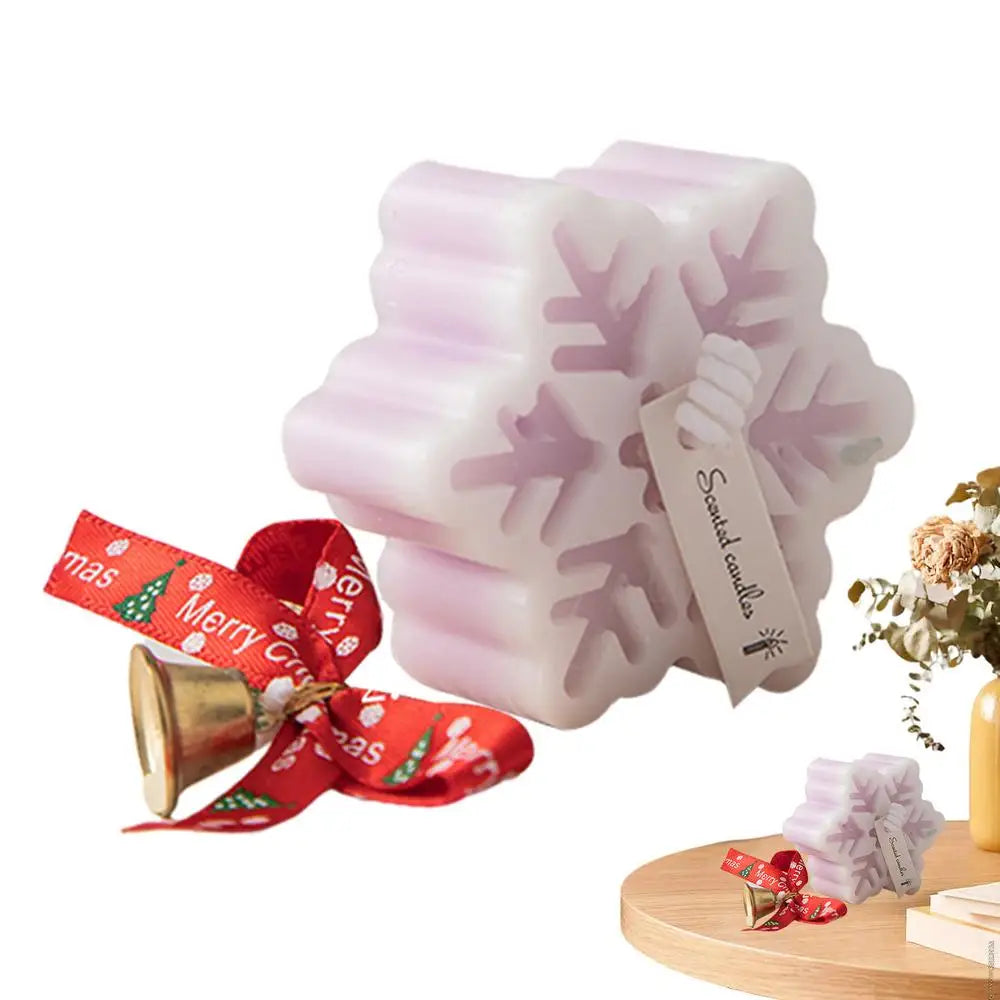 Snowflake-shaped scented candle with a label, accompanied by a red "Merry Christmas" ribbon and a golden bell, displayed on a wooden surface with floral decor.