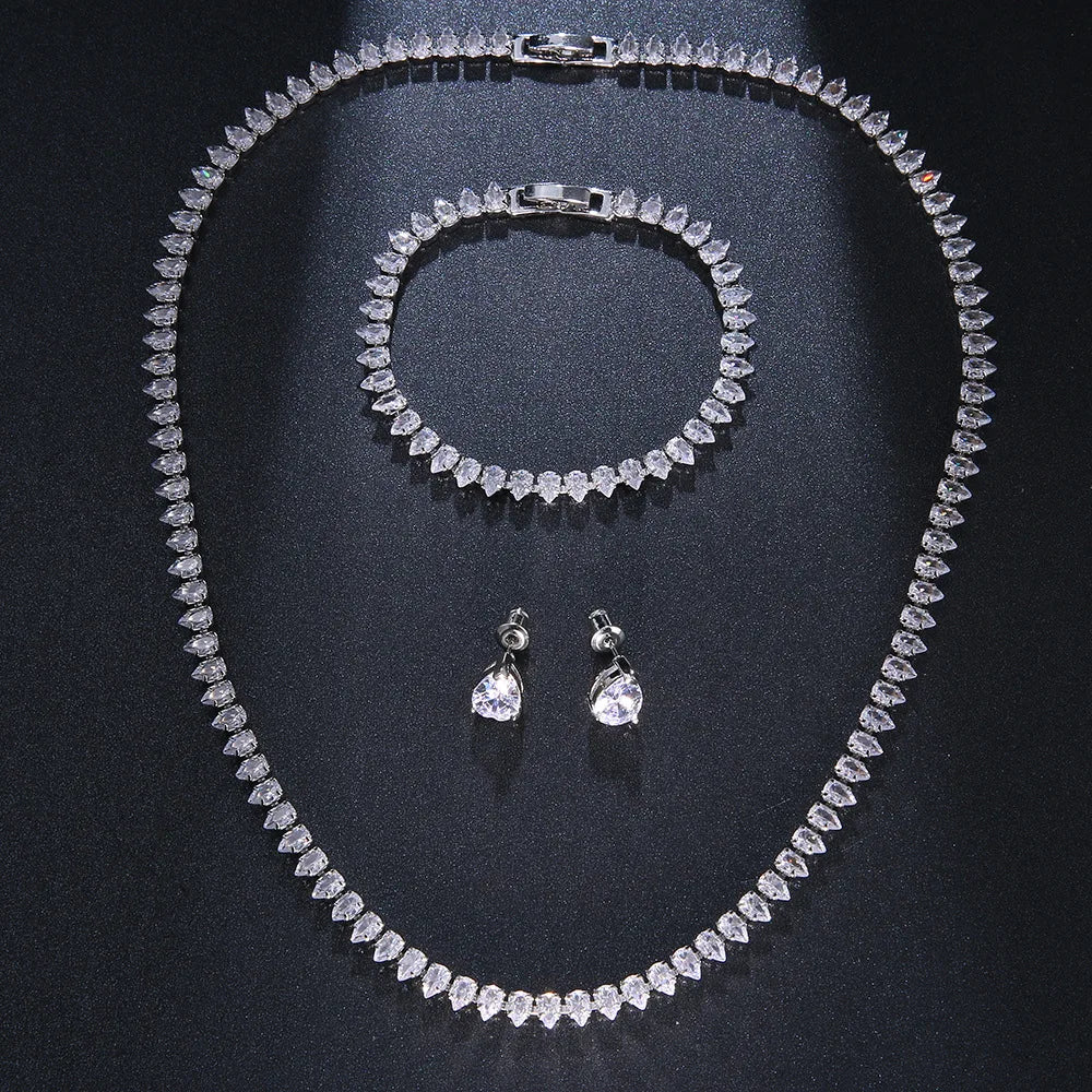 Diamond jewelry set with a teardrop design against a dark background, featuring a necklace, bracelet, and earrings elegantly arranged.