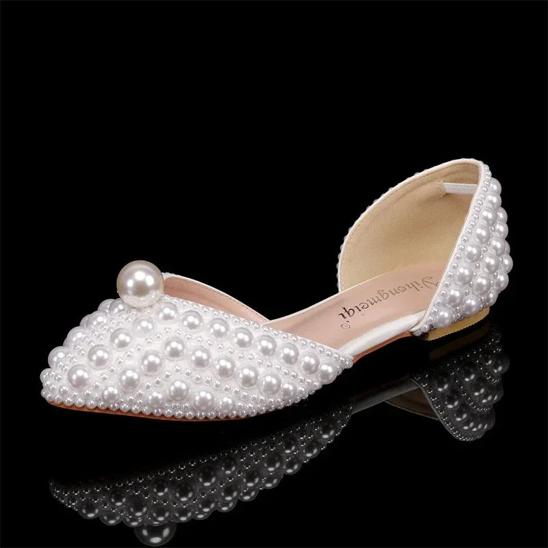 Elegant flat shoe adorned with small white pearls and a large pearl accent on the toe, set against a glossy black background.