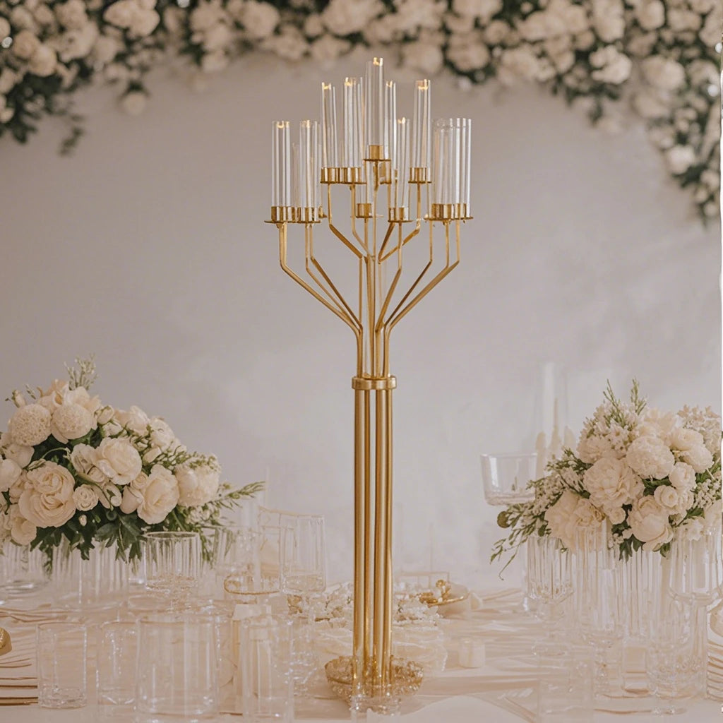 Elegant table display with a tall gold candelabra, surrounded by white floral arrangements and glassware. A lush floral backdrop enhances the sophisticated ambiance.