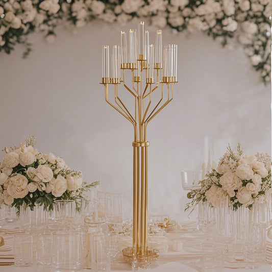 Elegant table display with a tall gold candelabra, surrounded by white floral arrangements and glassware. A lush floral backdrop enhances the sophisticated ambiance.