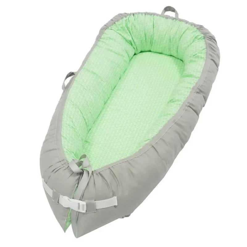 A soft, light green and gray baby lounger with padded sides, designed for comfort. It features adjustable straps and handles, providing secure and portable use for infants.