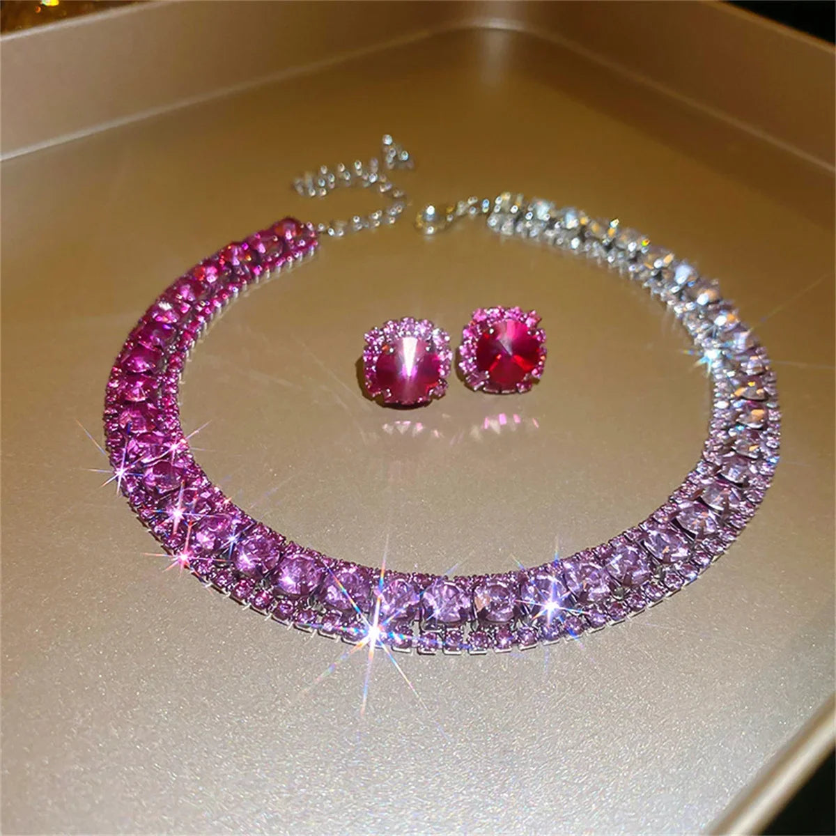 Sparkling necklace with pink gemstones and matching pink stud earrings on a gold surface, reflecting light and creating a shimmering effect.