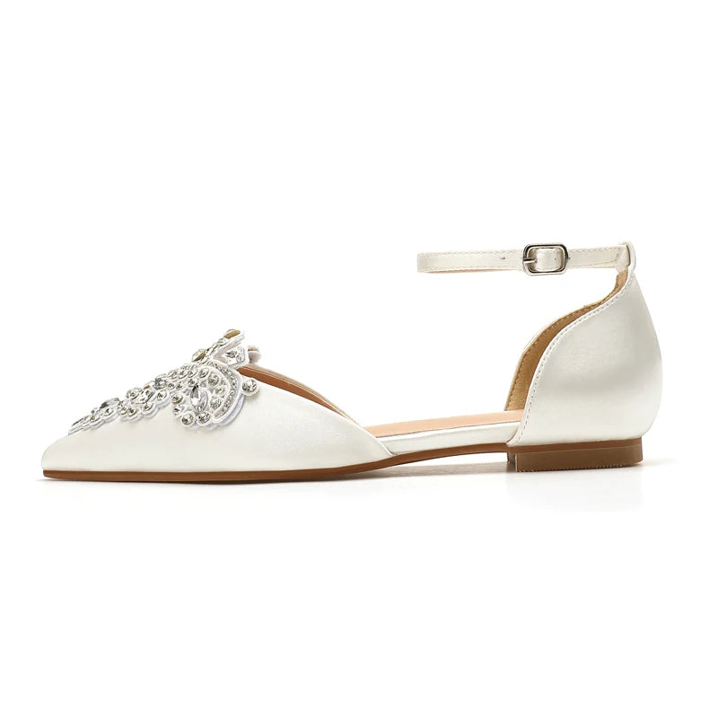 Elegant white flat shoe with a pointed toe, detailed with sparkling crystal embellishments, and a delicate ankle strap.