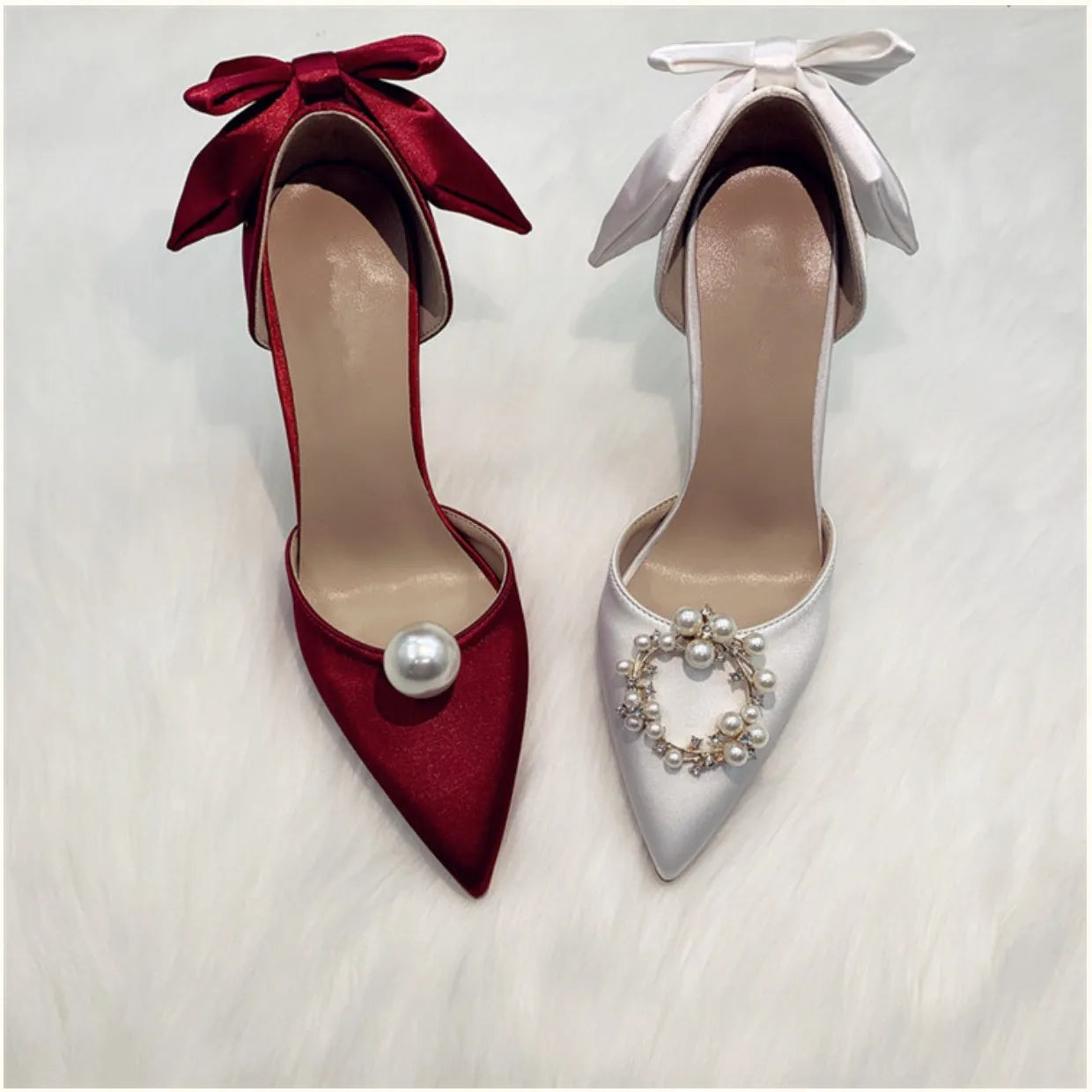 Two elegant high-heeled shoes on a white surface: one red with a large pearl, the other white adorned with a pearl wreath. Each features a matching bow on the heel.