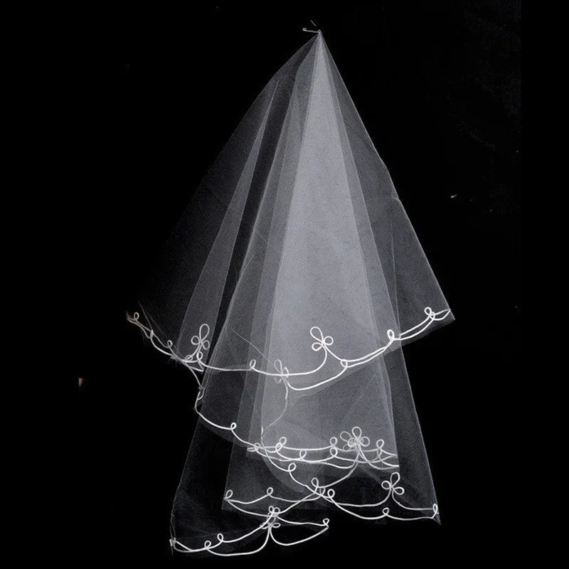 A delicate white bridal veil with intricate floral embroidery along the edges is set against a black background, highlighting its elegant and sheer design.