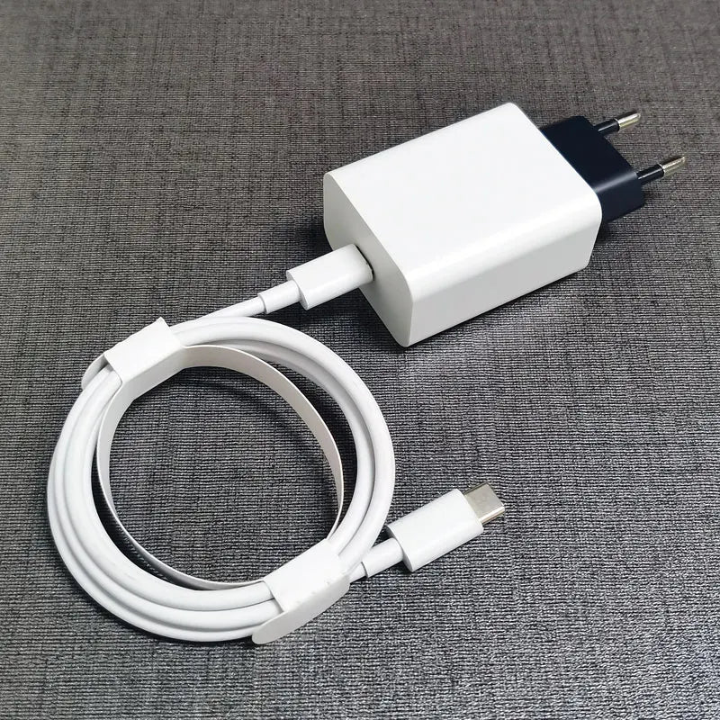White USB-C charger with a coiled cable on a gray textured surface. The plug has two round prongs, and the charger is connected to the cable.