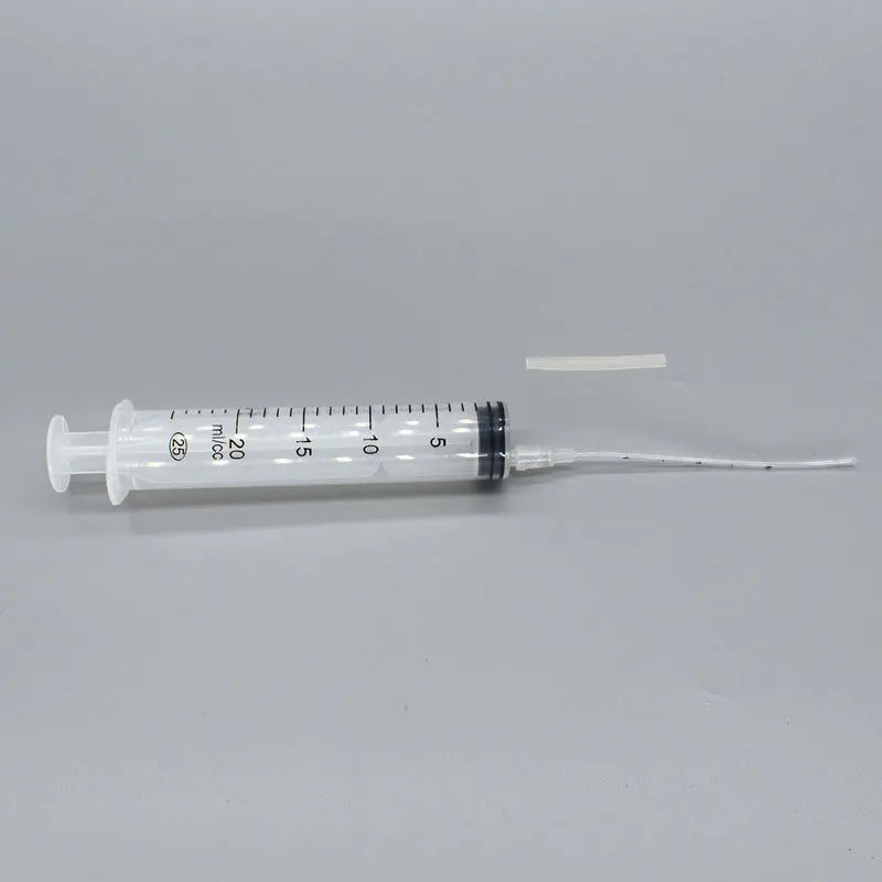 A 20 ml clear plastic syringe with measurement markings and a long, thin nozzle is placed on a gray surface.