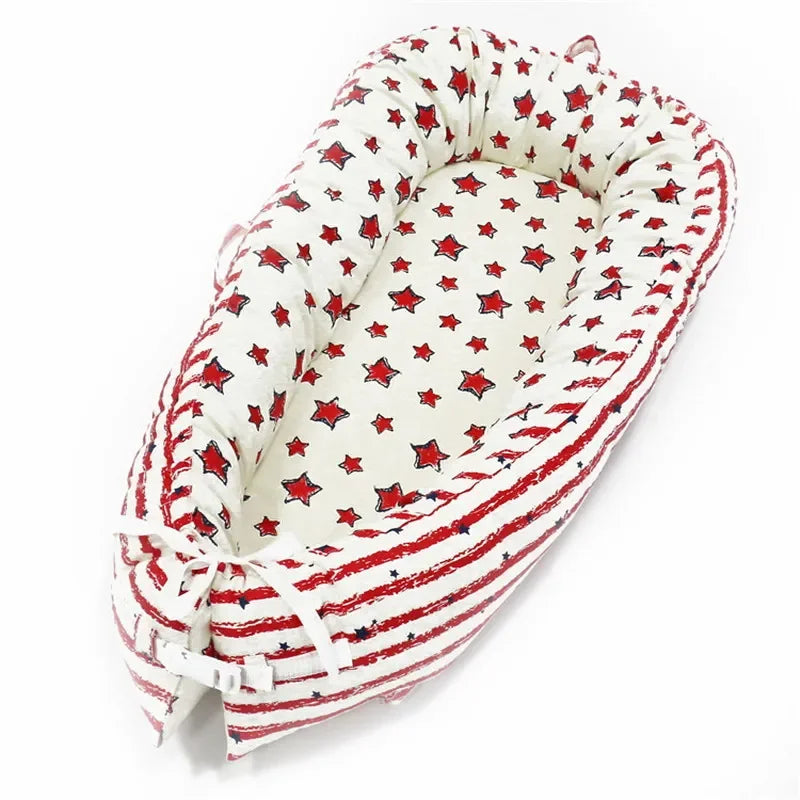 Cozy baby nest with a star pattern, featuring red and blue stars on a white background. The side padding shows red stripes, and the nest is tied with white fabric bows.