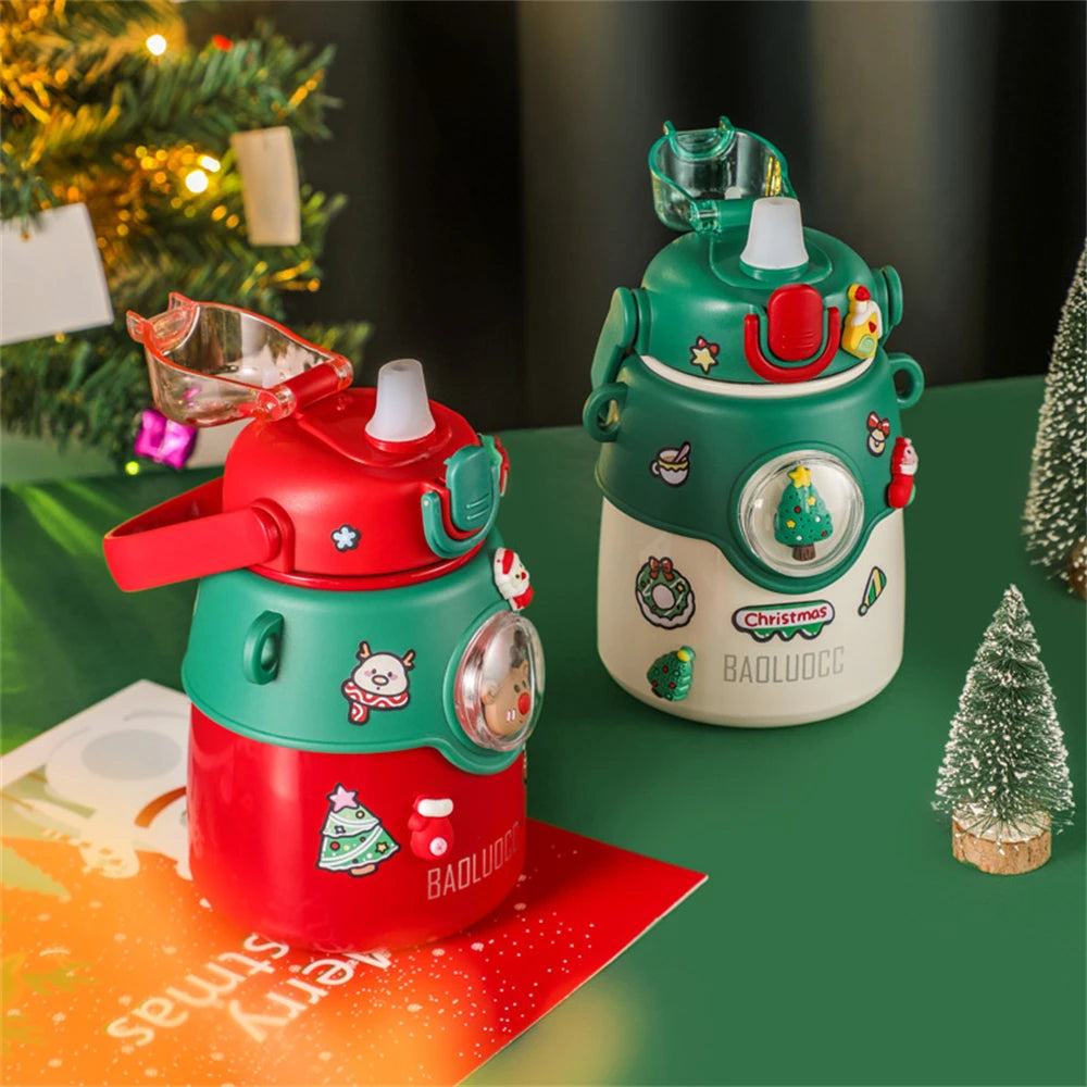 Two festive humidifiers, one red and green, the other green and cream, decorated with Christmas motifs, sit on a green table near a decorated tree and a small snow-covered tree.