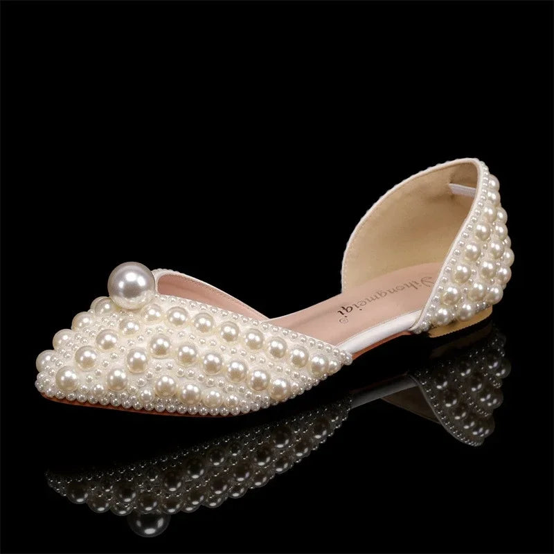 Elegant ivory flat shoe adorned with varying sizes of pearls across the toe and heel, set against a black background.