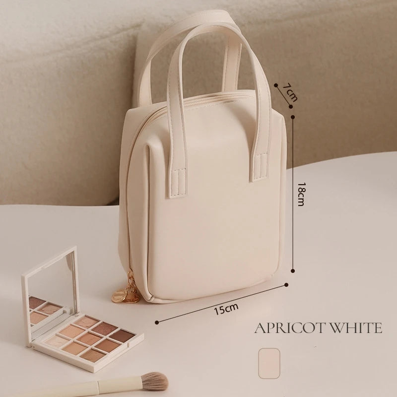 A small apricot white handbag with dimensions labeled 18cm by 15cm by 7cm, placed on a table with a neutral eyeshadow palette and makeup brush beside it.