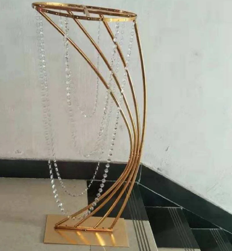 A curved, gold metal stand with draped crystal beads, set on a light-colored floor against a plain wall, creating an elegant and decorative display piece.