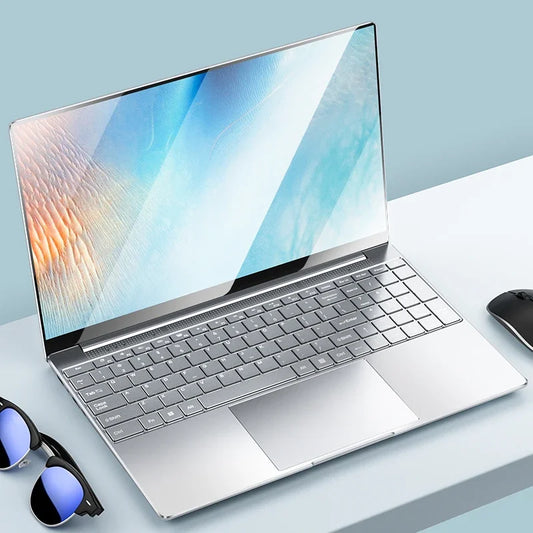 Sleek silver laptop on a light blue desk, displaying a colorful abstract screen. Nearby are sunglasses and a wireless mouse, creating a modern and stylish workspace setting.