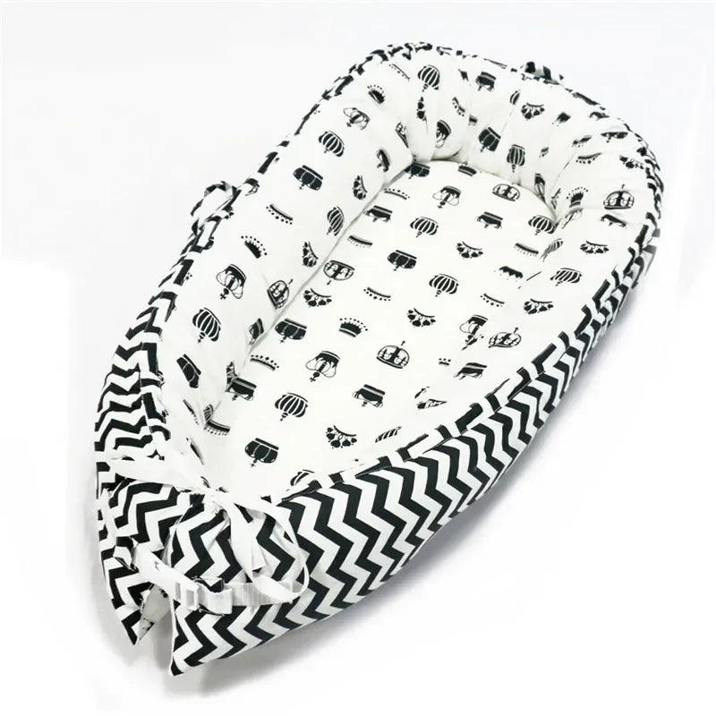 Black and white baby nest with zigzag pattern on the edge and small crown and carriage designs inside, tied with a white ribbon at the bottom.