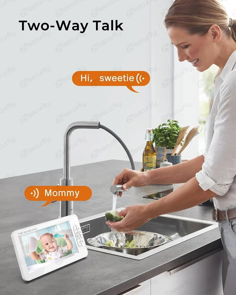 A woman in a kitchen smiles while using a two-way talk feature on a baby monitor. The monitor displays a baby and has speech bubbles saying "Hi, sweetie" and "Mommy."