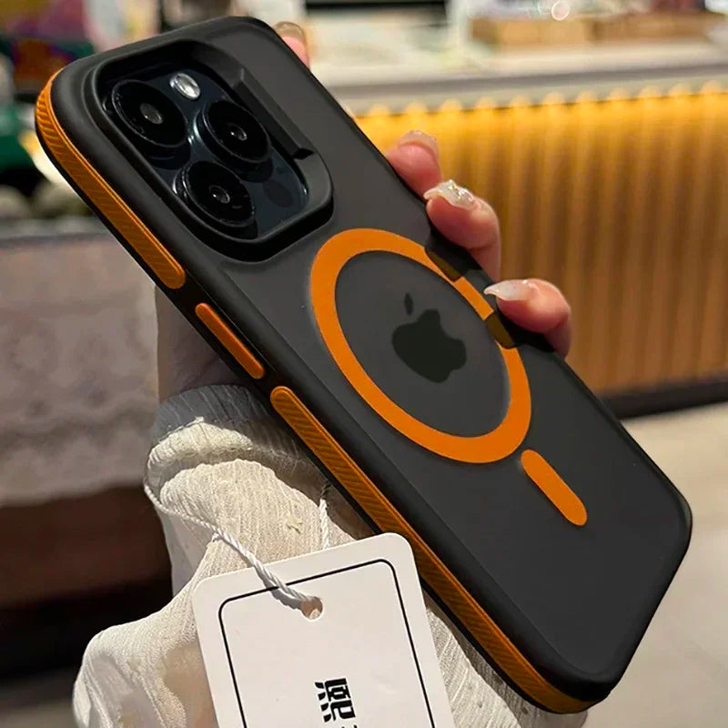 A hand holds a smartphone with a black and orange protective case featuring a circular design around the Apple logo. A white tag with text is attached to the case.