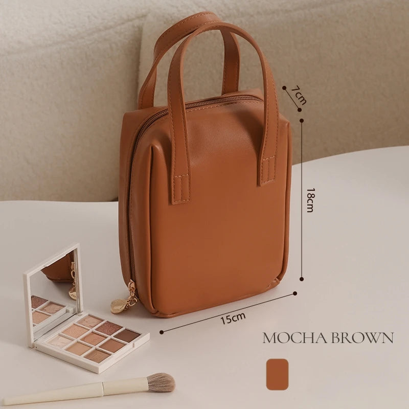 Mocha brown handbag standing upright on a table, measuring 18cm by 15cm by 7cm. In the foreground, a neutral eyeshadow palette and brush are placed beside it.