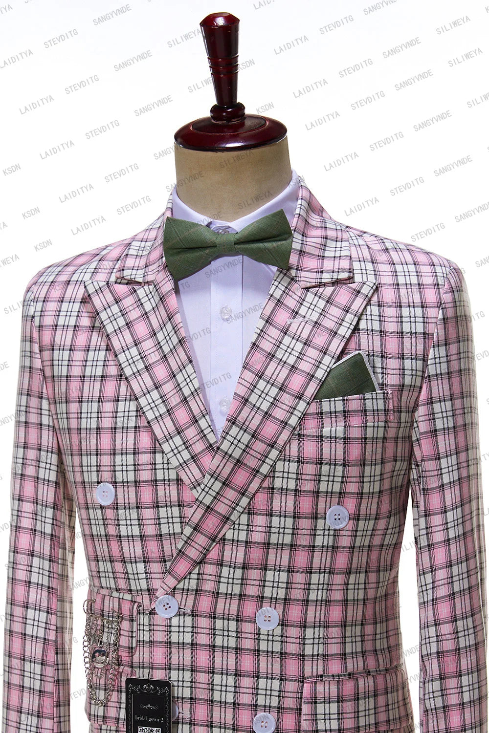 A mannequin dressed in a pink plaid double-breasted suit with white buttons, featuring a green pocket square and bow tie, and adorned with silver chain details.