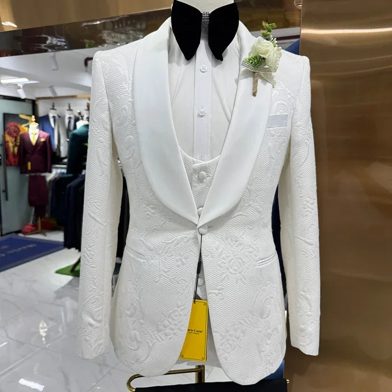 White textured tuxedo with a black bow tie, floral boutonniere, and a waistcoat is displayed in a bright store. Other suits are visible in the background.