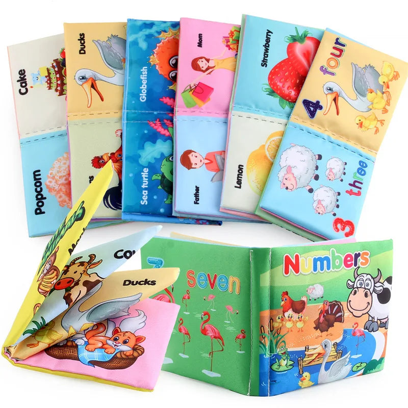 Colorful children's cloth books featuring illustrations of animals, fruits, and numbers. Titles include "Ducks," "Numbers," and "Sea Turtle." Books are arranged in a fan shape.