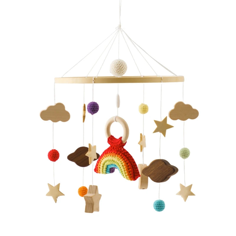 Hanging baby mobile featuring a crocheted rainbow centerpiece, surrounded by wooden stars, clouds, and colorful crocheted balls on strings, attached to a wooden hoop.