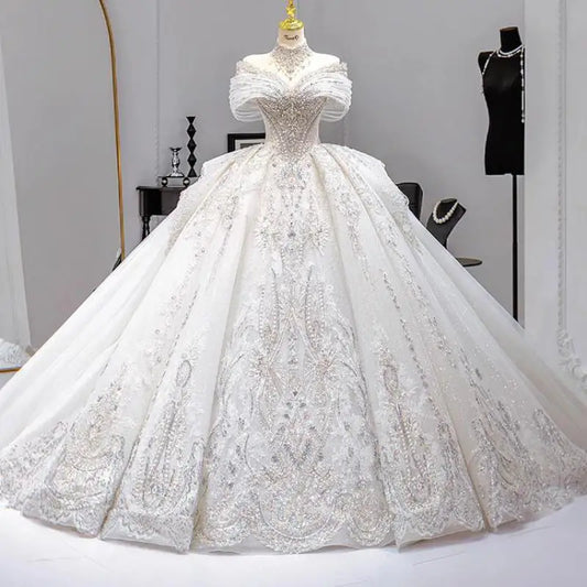 Elegant white ball gown with intricate lace details on a mannequin in a chic boutique. The dress features an off-the-shoulder neckline and a voluminous skirt, surrounded by accessories.