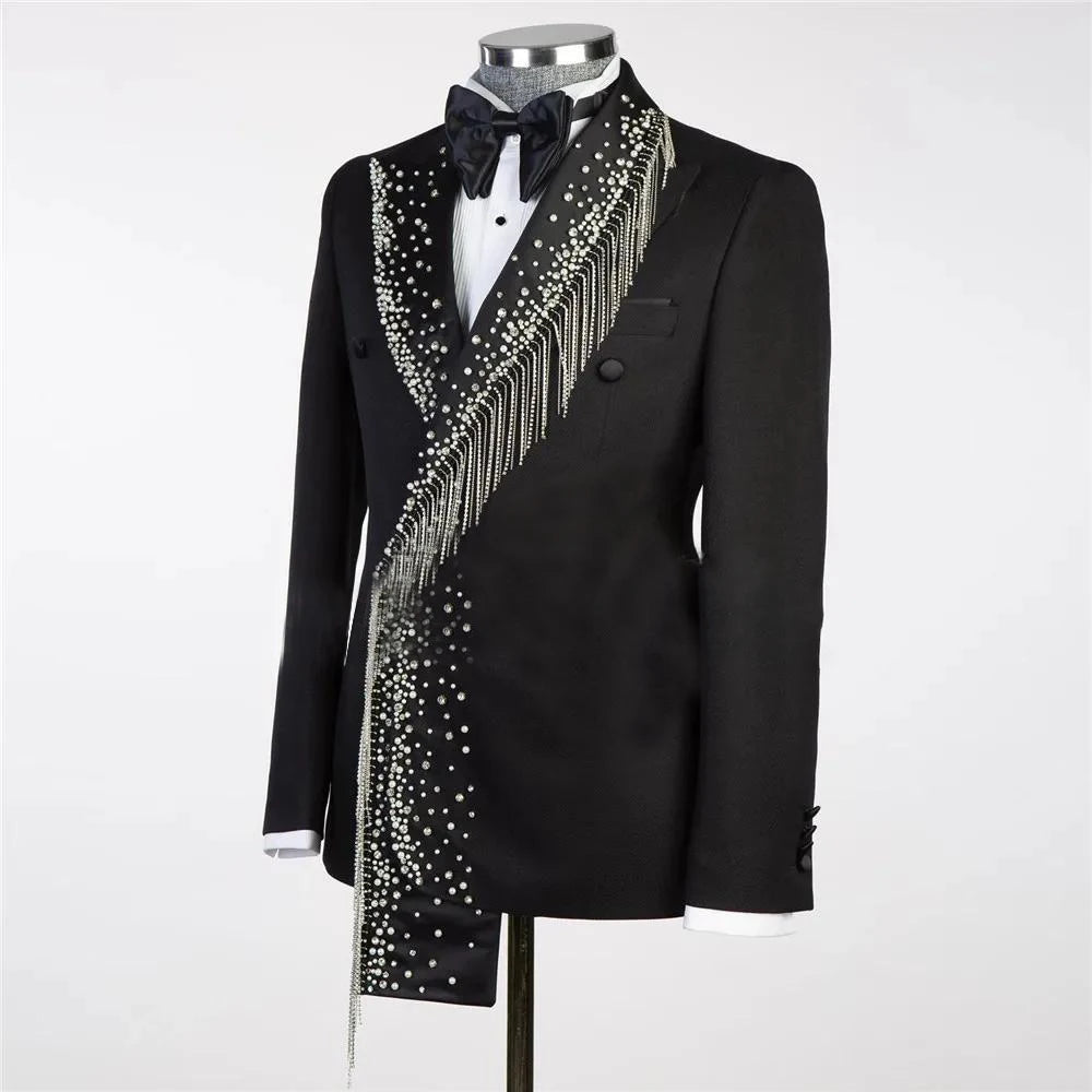A black double-breasted tuxedo jacket adorned with cascading pearls and fringe on the left side, paired with a crisp white shirt and a black bow tie on a mannequin.