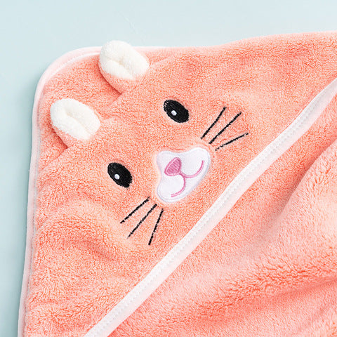 A soft, peach-colored towel with an animal face design, featuring embroidered eyes, whiskers, a pink nose, and plush ears. The background is a pale blue surface.