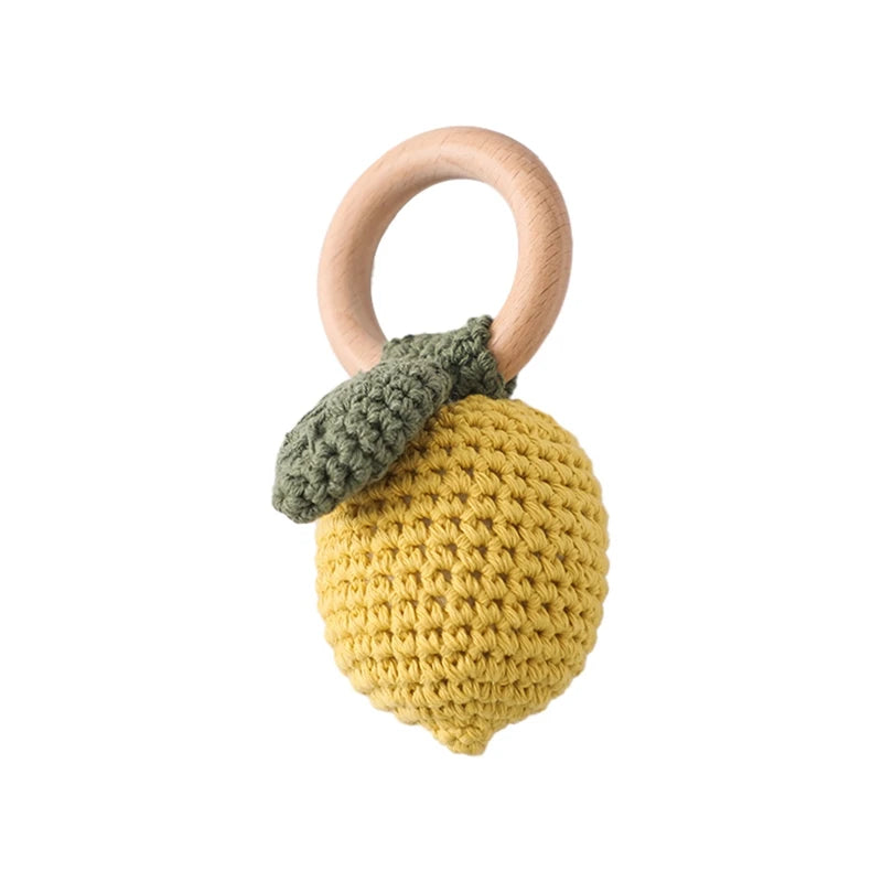 Crocheted yellow lemon with a green leaf attached to a wooden ring, resembling a playful baby rattle toy on a white background.