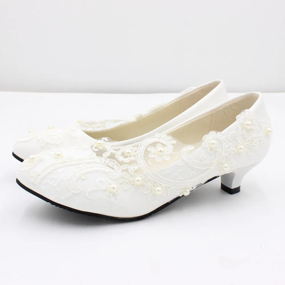 Elegant white low-heel shoes adorned with delicate lace and small pearl accents, set on a clean, white background.