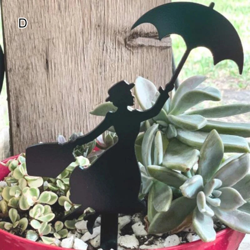 Silhouette of a figure holding an umbrella and bag, placed among green succulents in a red pot. A rustic wooden background and greenery are visible.