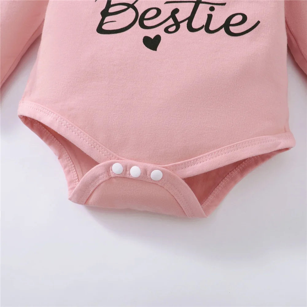 Pink baby onesie with "Bestie" text and a small heart, featuring long sleeves and three white snap buttons at the crotch.