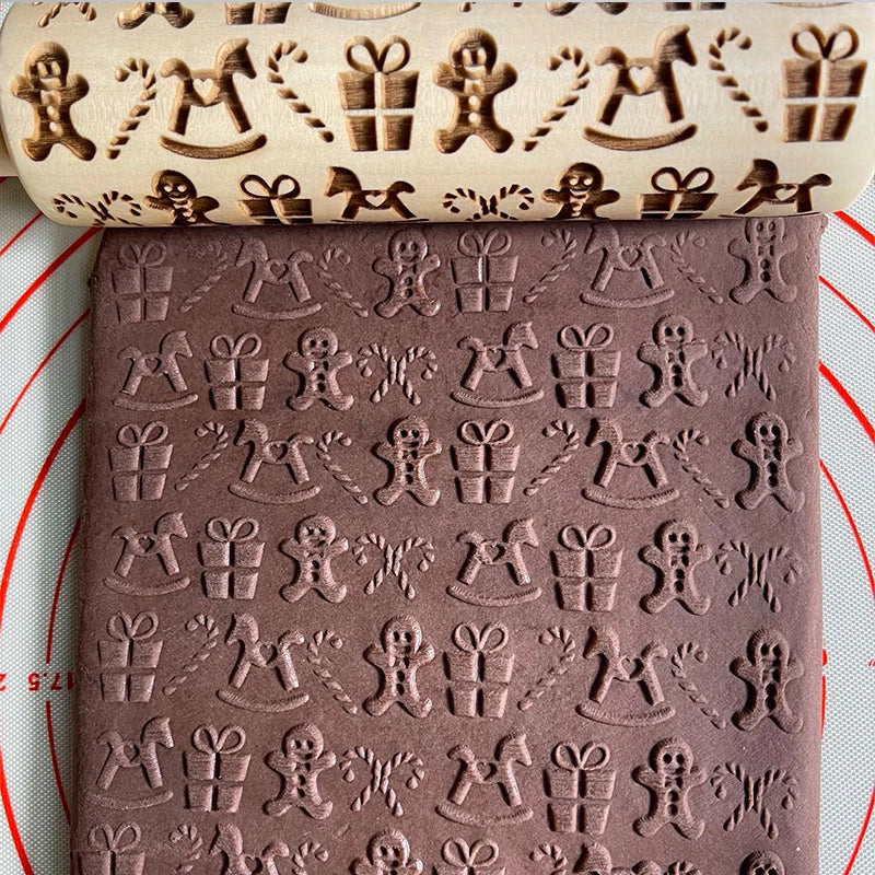 Embossed rolling pin and chocolate dough with festive designs: gingerbread men, rocking horses, wrapped gifts, and candy canes on a circular white and red silicone mat.