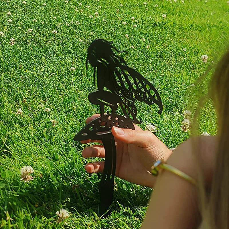 Silhouette of a fairy with wings sitting on a mushroom, held by a person on a grassy field dotted with white clover flowers.