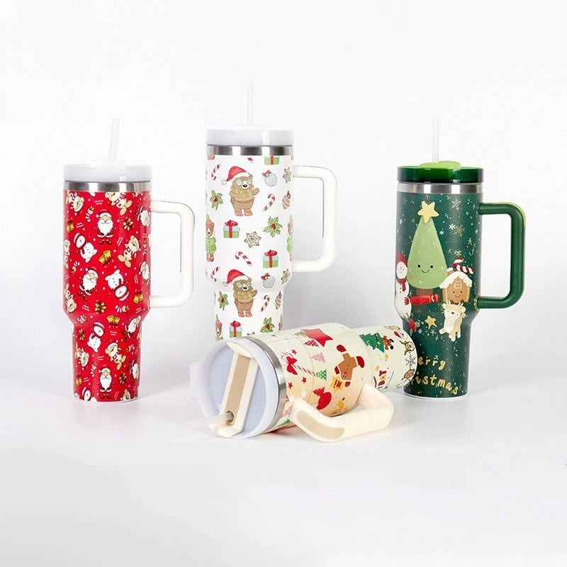 Four festive travel mugs with handles and straws, featuring Christmas-themed patterns with Santa, snowmen, trees, and gifts. Various colors: red, white, and green.