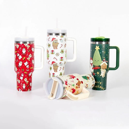 Four festive travel mugs with handles and straws, featuring Christmas-themed patterns with Santa, snowmen, trees, and gifts. Various colors: red, white, and green.