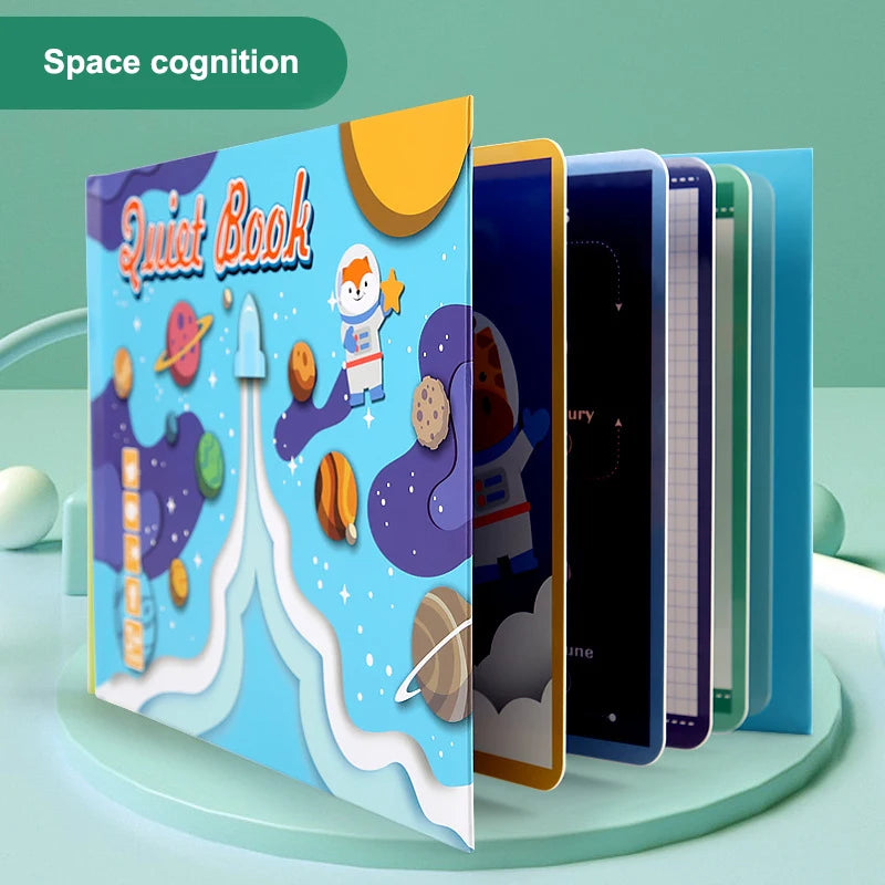 Children's book titled "Quiet Book" with a space theme, featuring an astronaut, planets, and rockets on a colorful cover. The book is open, showing multiple pages.