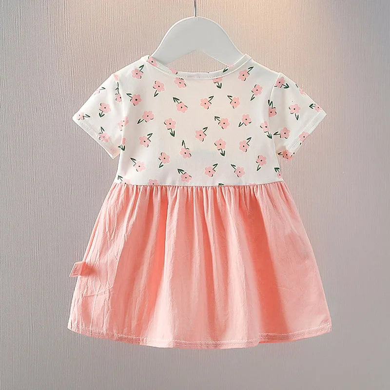 A small child's dress with a white floral-patterned top and a pink skirt, displayed on a hanger against a light background.