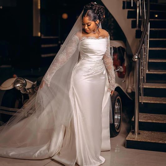 Bride in an elegant satin wedding dress with lace sleeves and a long veil, standing near a vintage car by a staircase. Her hair is styled in an elaborate updo.