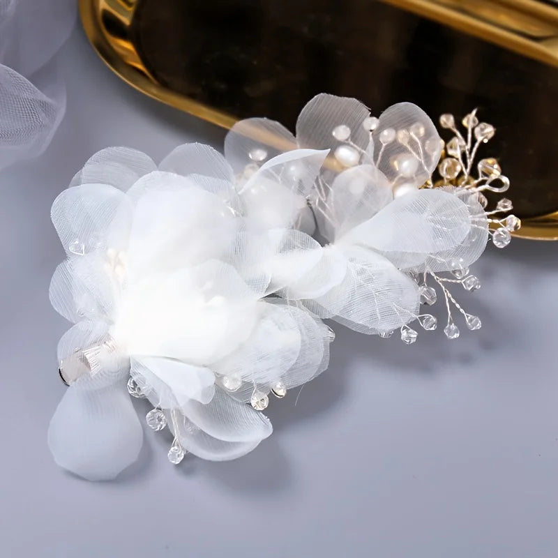 Delicate white floral hair clip with fabric petals, pearl beads, and crystal-like accents on a metallic surface.