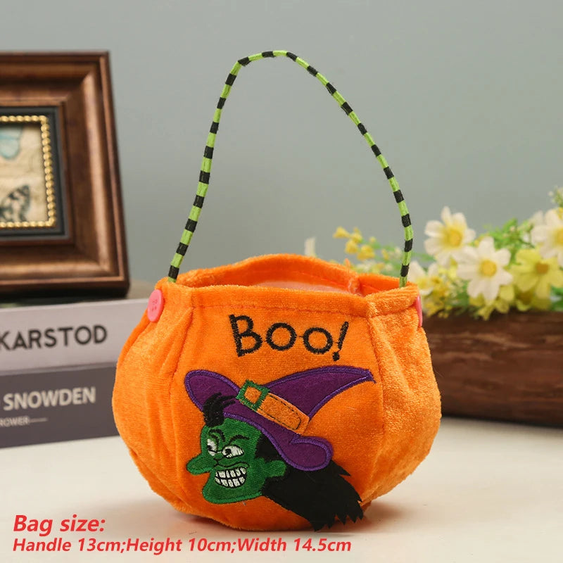 Bright orange Halloween bag with "Boo!" text and a green witch head embroidered. Features a striped handle and button accents. Books and flowers are in the background. Bag size listed below.