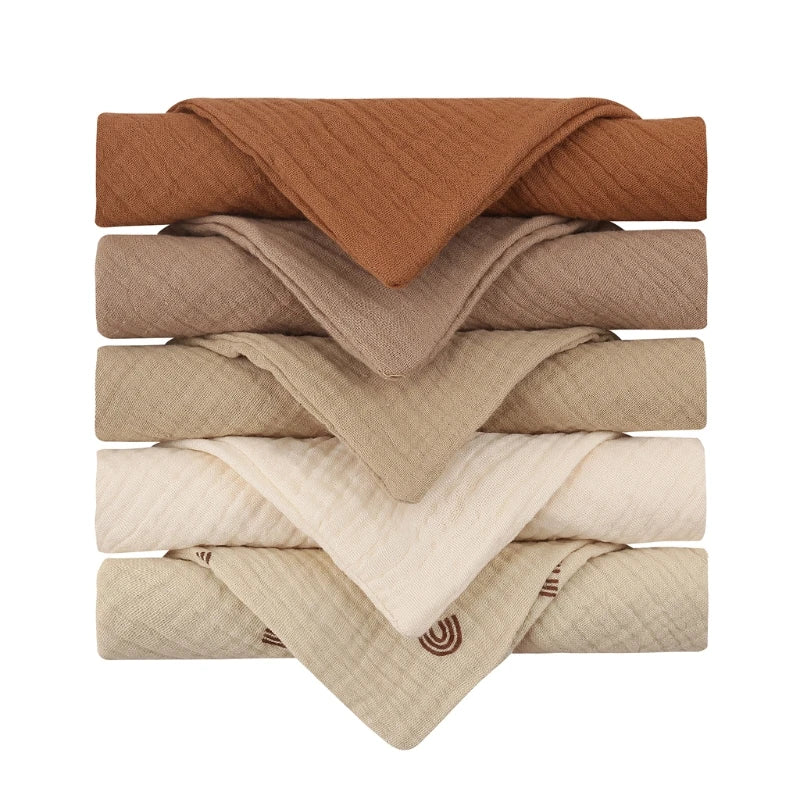 A stack of six folded, earth-toned blankets in shades of brown, beige, and tan. The bottom blanket features a subtle pattern. Each blanket is neatly arranged in a layered fashion.