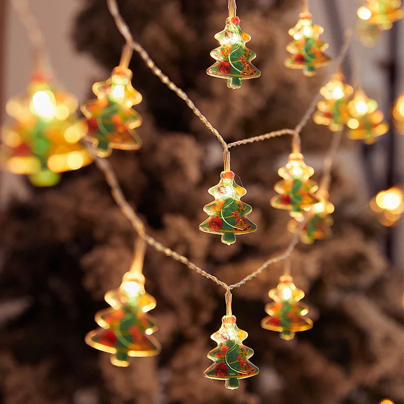 String lights shaped like Christmas trees glow warmly against a blurred background, creating a festive atmosphere with green and red decorations.