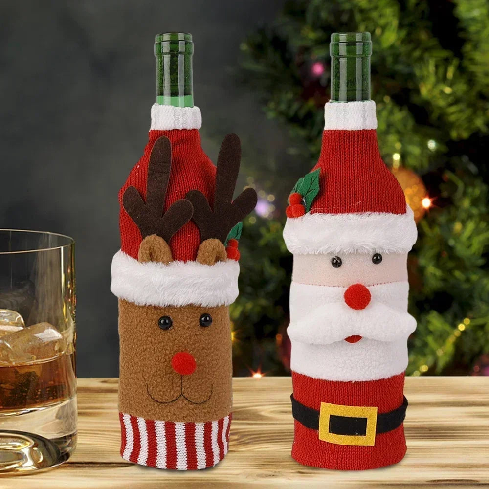 Two wine bottles dressed as a reindeer and Santa Claus, with a glass of whiskey nearby. A Christmas tree with lights is in the background.