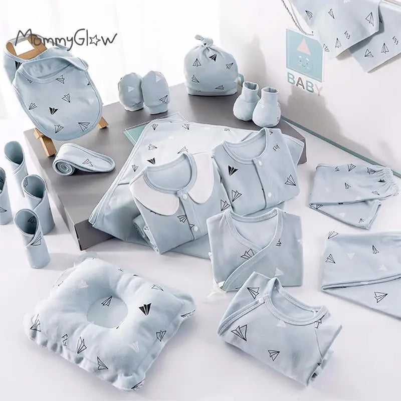 A collection of baby clothing and accessories in light blue, featuring paper airplane patterns. Includes onesies, mittens, a pillow, and a beanie, neatly arranged on a surface.