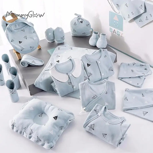 A collection of baby clothing and accessories in light blue, featuring paper airplane patterns. Includes onesies, mittens, a pillow, and a beanie, neatly arranged on a surface.
